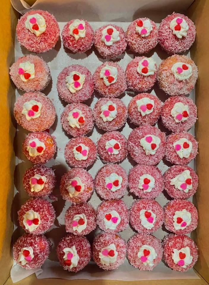 A box of pink coconut cupcakes topped with cream and sugar hearts