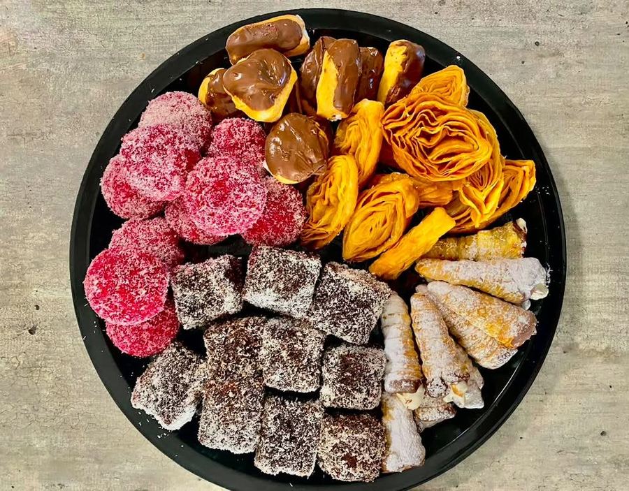 Dessert platter with chocolate éclairs, pink coconut balls, lamingtons, cream horns and pastry roses